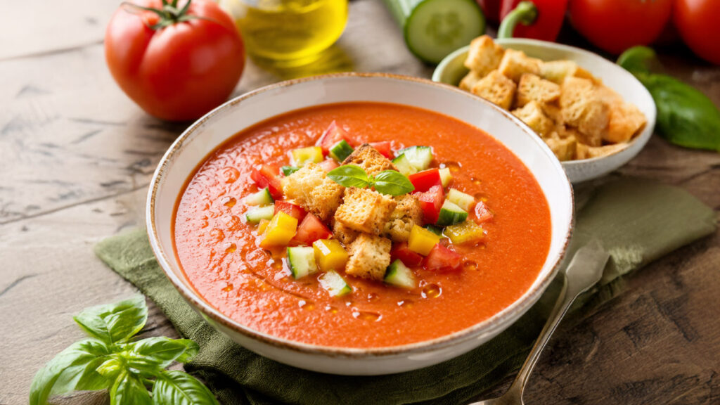 Gazpacho andaluso servito freddo con crostini di pane dorati, verdure fresche e filo di olio extravergine d'oli
